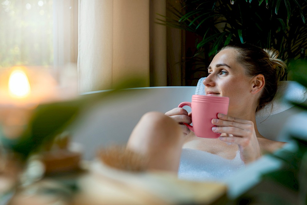 Young woman relaxing in a bubble bath holding a pink mug