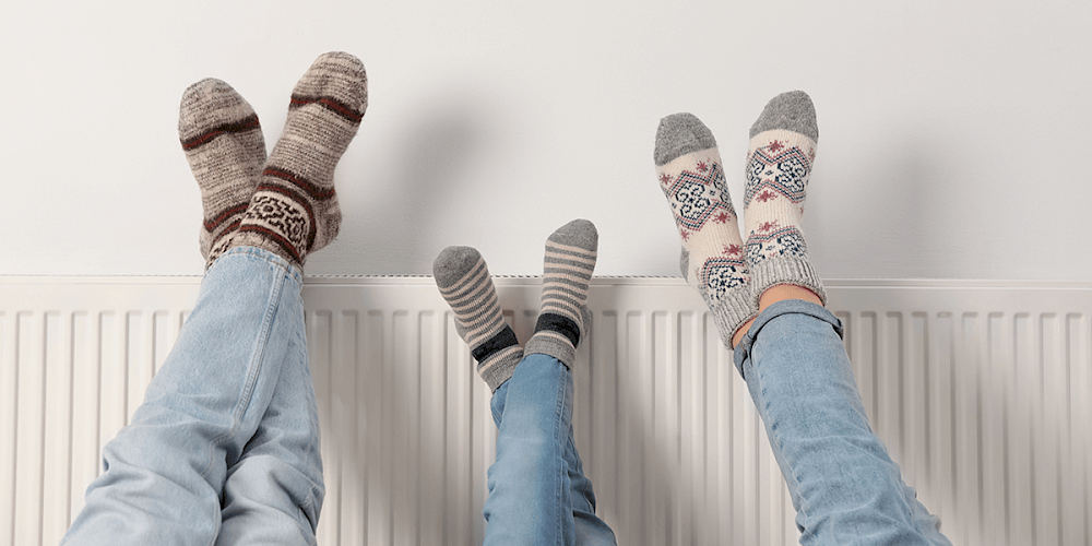 Three pairs of feet with winter socks resting against a white radiator